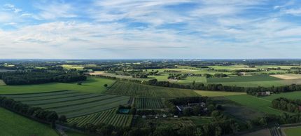 Luchtfoto van groene landbouwgrond en velden onder een blauwe hemel met verspreide wolken.