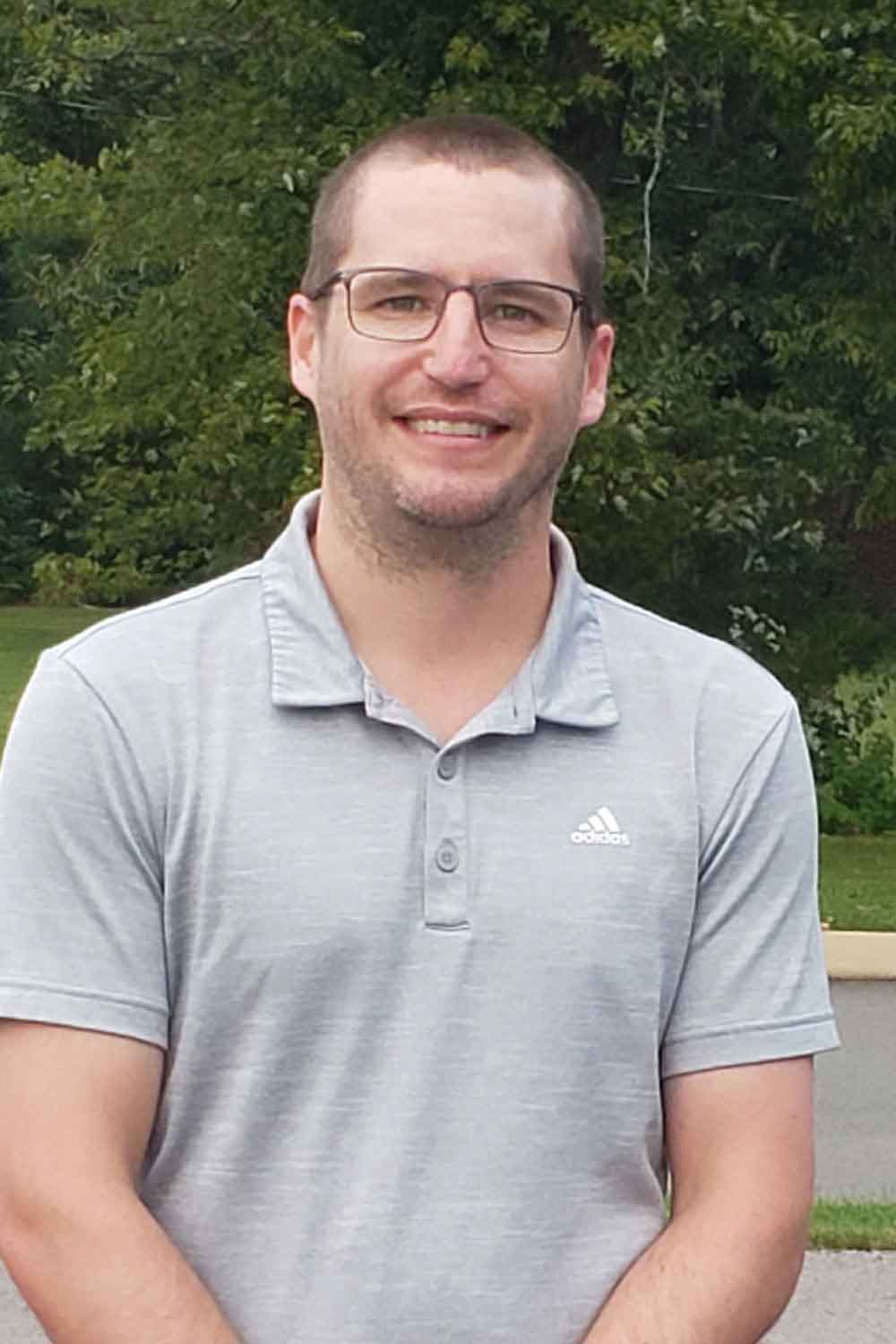 A man wearing glasses and a grey polo shirt is smiling for the camera.