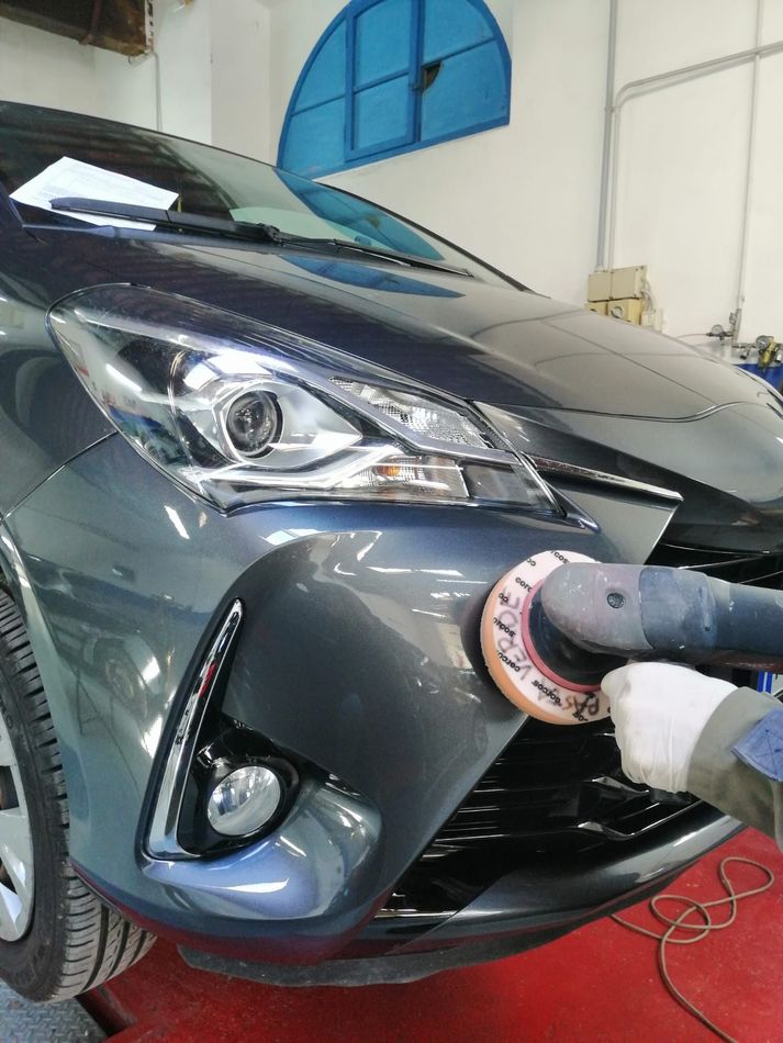 Un'auto grigia viene lucidata con una lucidatrice in un'officina.