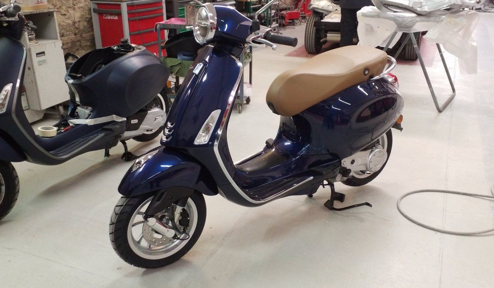 Scooter blu con sella color cuoio parcheggiato all'interno di uno showroom.