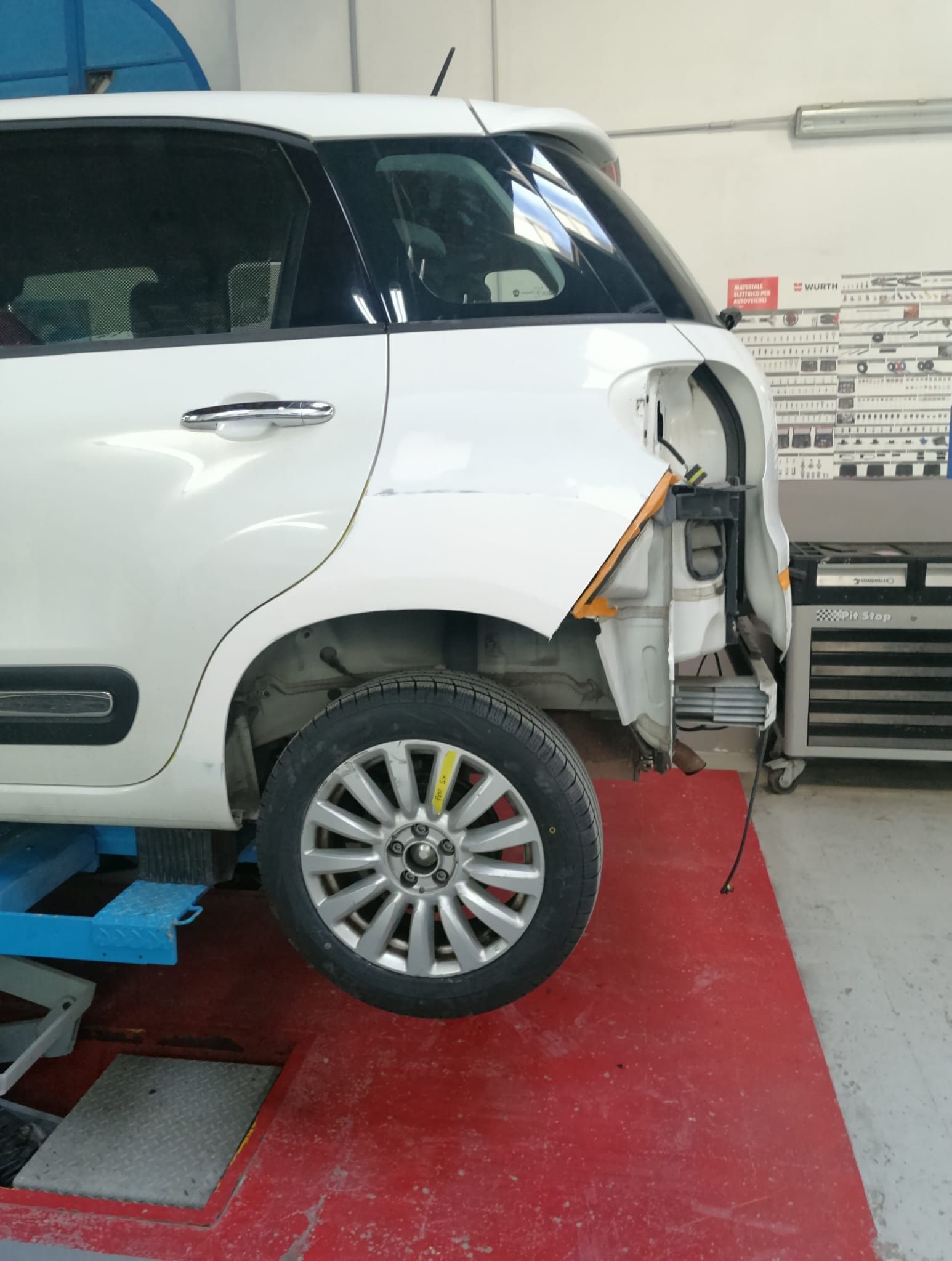 Un SUV bianco è in riparazione presso un'officina meccanica, con il pannello laterale posteriore rimosso e la ruota a vista.