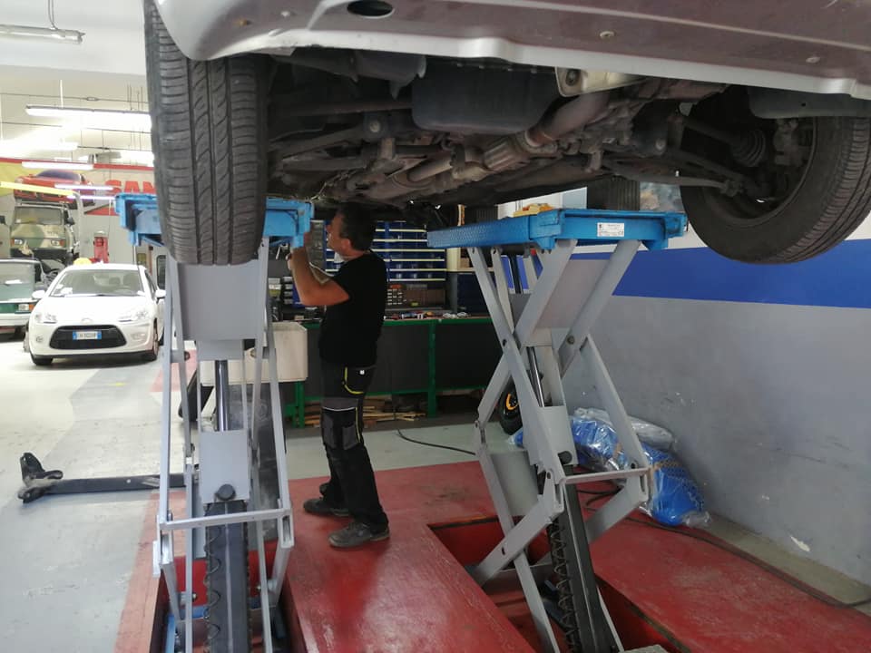 Meccanico al lavoro sotto un'auto su un ponte sollevatore in un'officina meccanica.