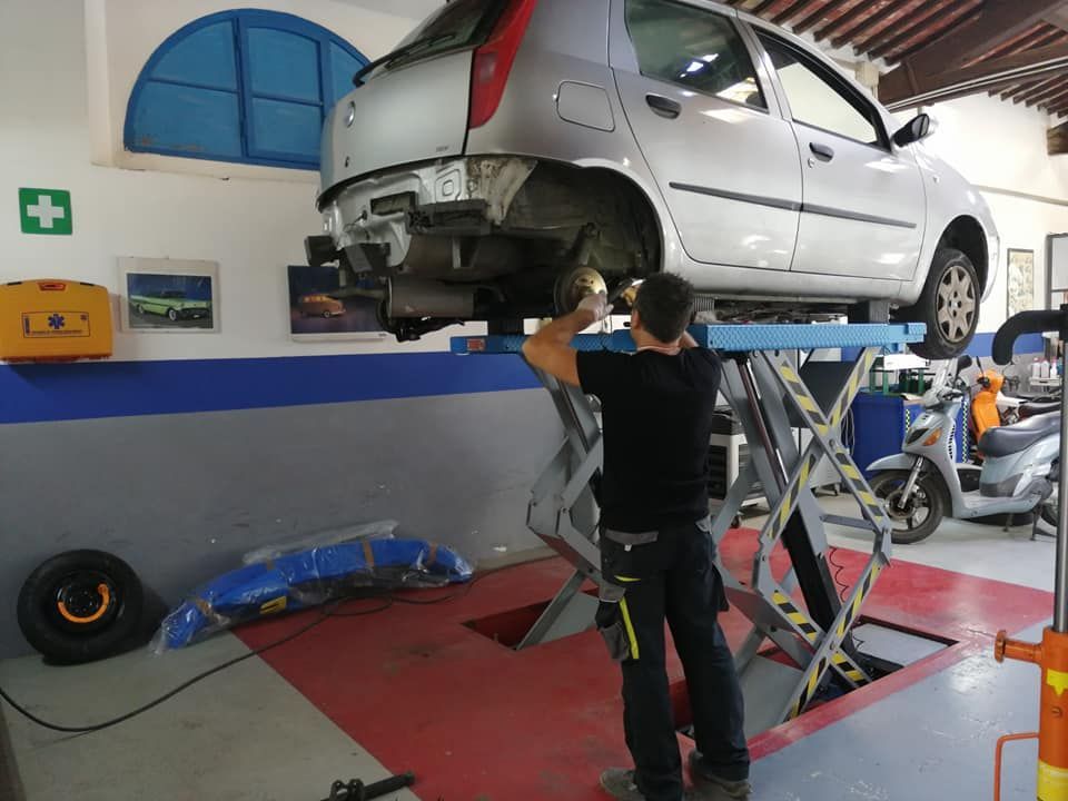 Un meccanico lavora sotto un'auto argentata sollevata su un ponte in un'officina meccanica.