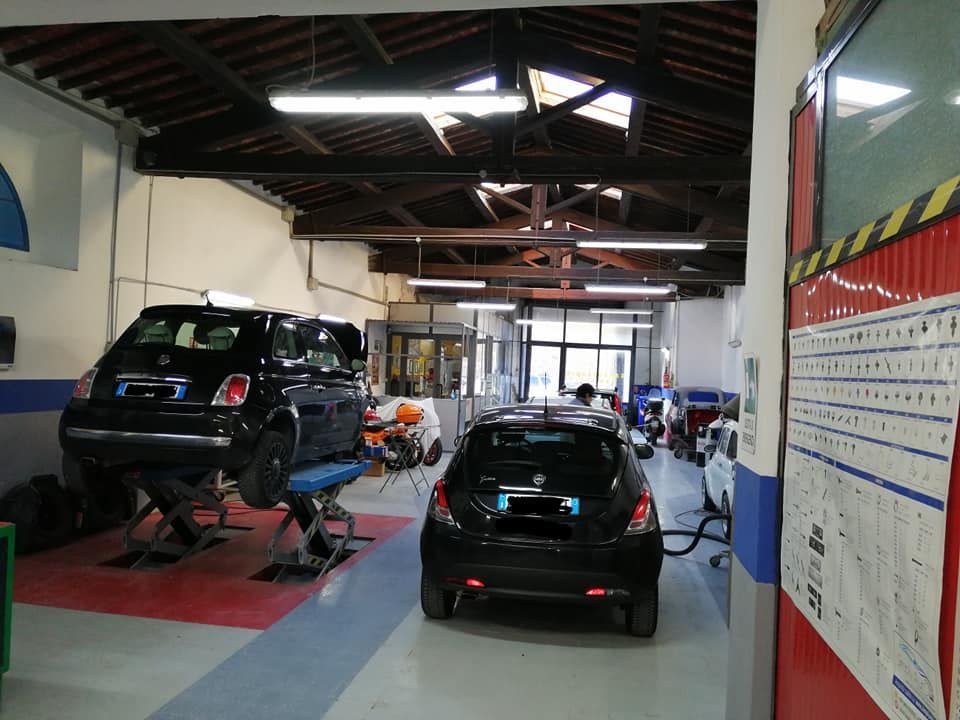 Officina meccanica con diverse auto sui ponti sollevatori e nelle postazioni di servizio, illuminate da luci intense.