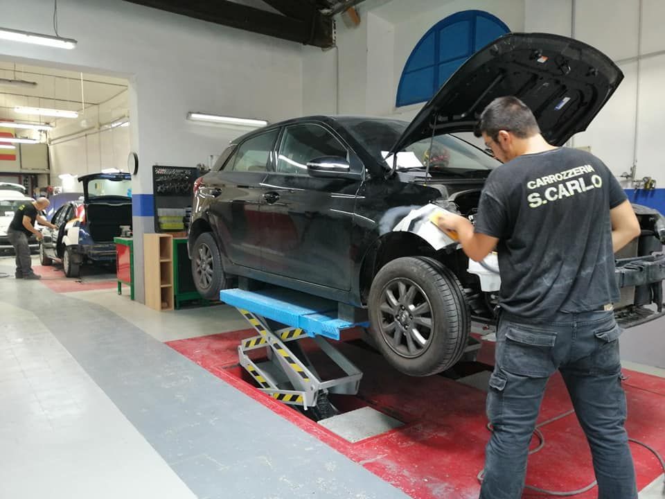 Un'auto nera sollevata su un ponte in un garage mentre un meccanico lavora sulla ruota anteriore.