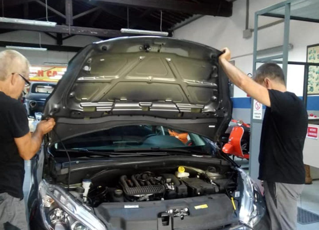 Due meccanici ispezionano un'auto con il cofano aperto in un'officina.