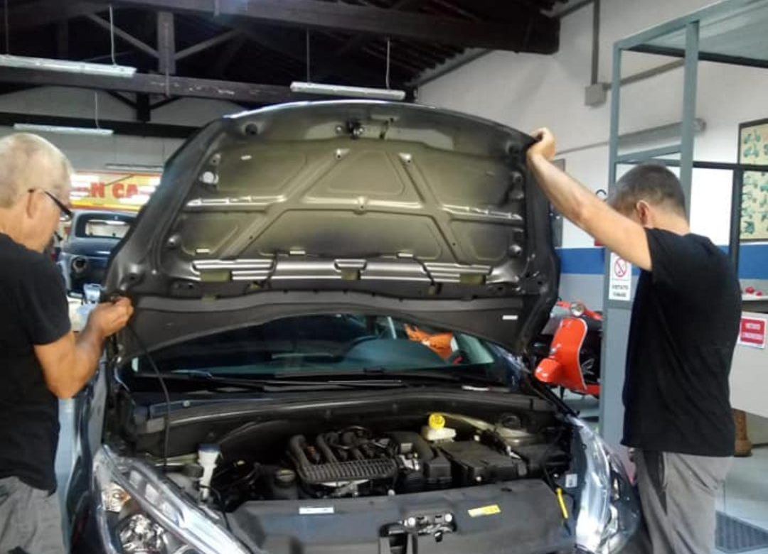 Due uomini lavorano su un'auto con il cofano aperto in un'officina.
