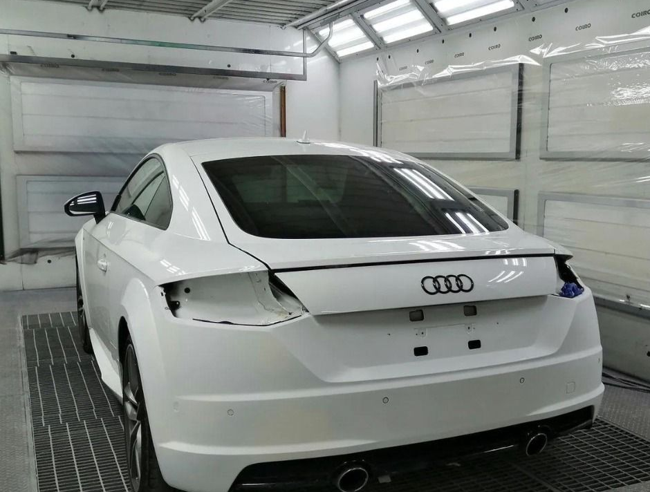Berlina Audi bianca in un garage, vista posteriore, con bagagliaio aperto e fanali posteriori rimossi per riparazione.