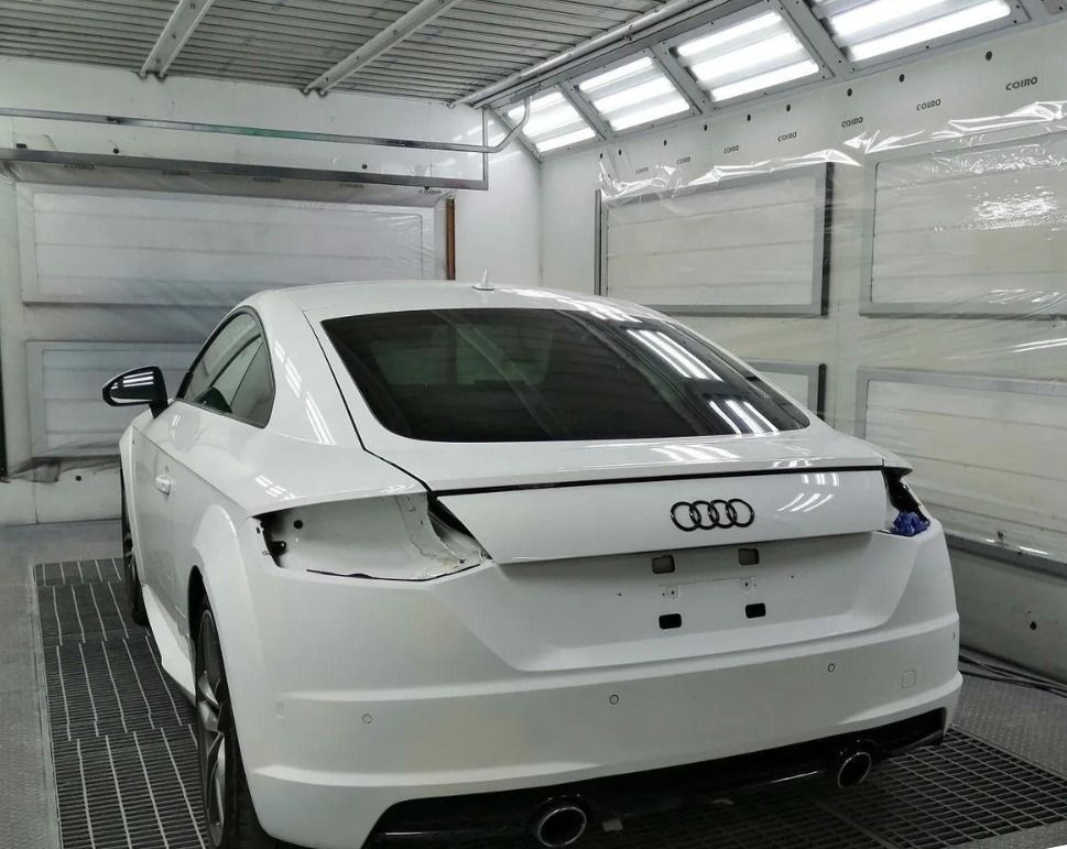 Berlina Audi bianca in una luminosa carrozzeria, vista posteriore con zona del fanale posteriore danneggiata.