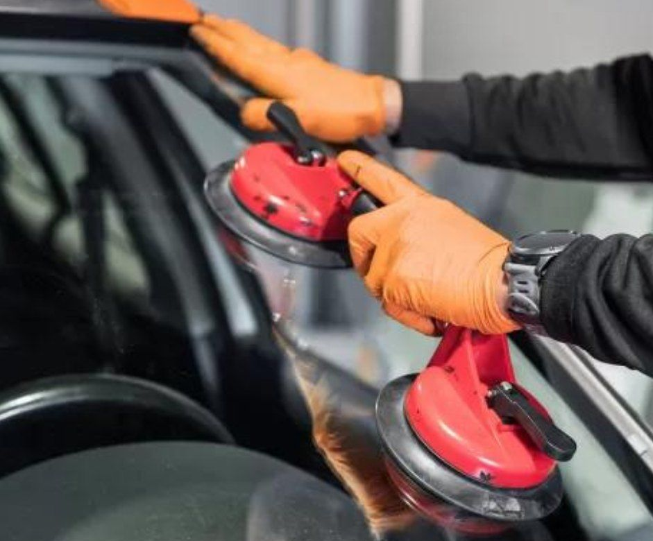 Mani con guanti arancioni che utilizzano ventose per rimuovere il parabrezza di un'auto.
