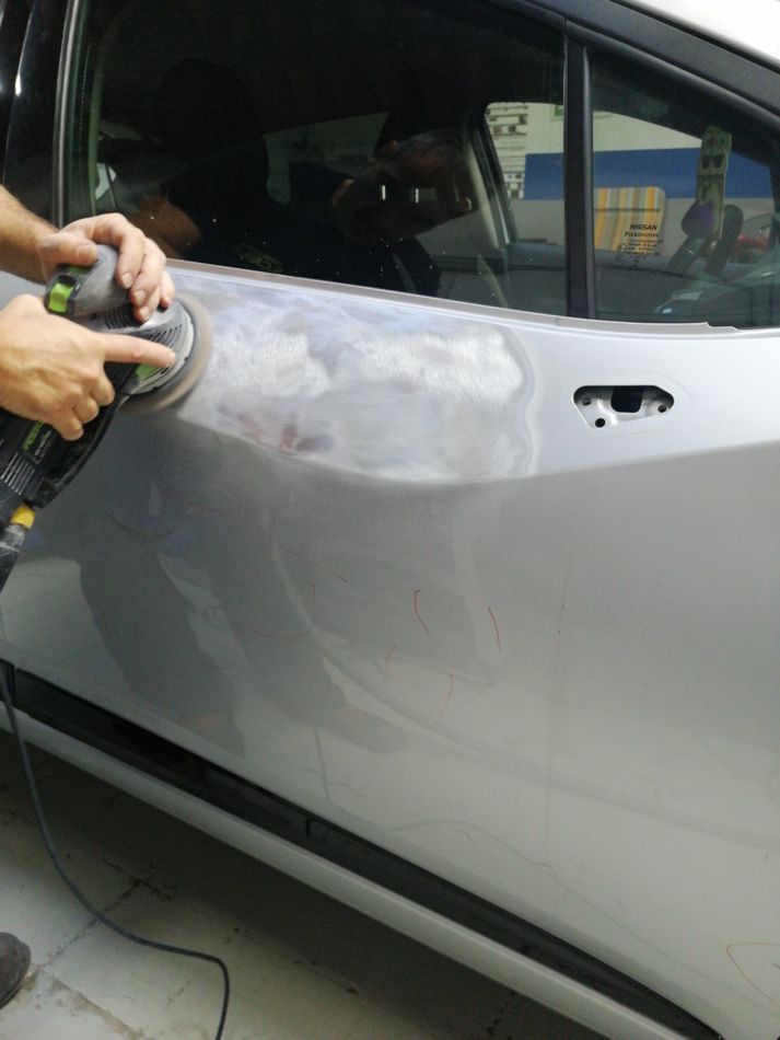 Una persona sta levigando la portiera argentata di un'auto con una levigatrice elettrica.