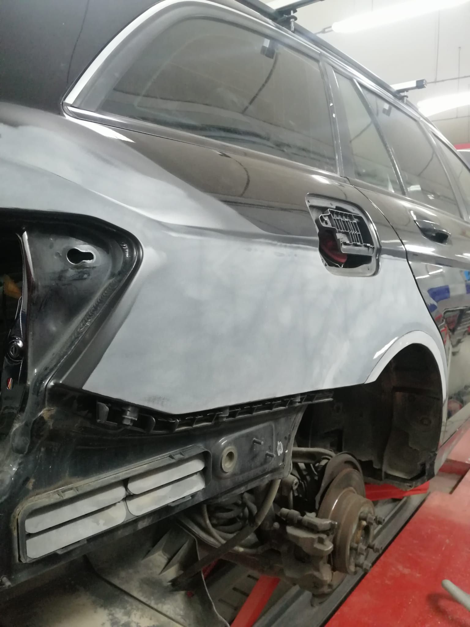 SUV argentato danneggiato in un'officina, ruota posteriore rimossa e pannelli della carrozzeria esposti.