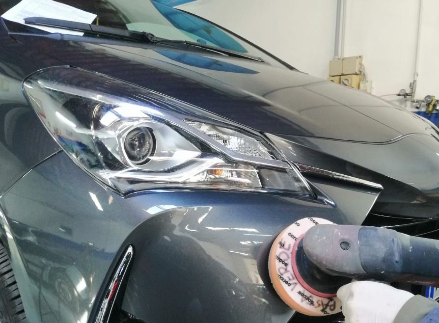 Primo piano di un'auto grigia lucidata con una lucidatrice sul paraurti anteriore e sul faro.