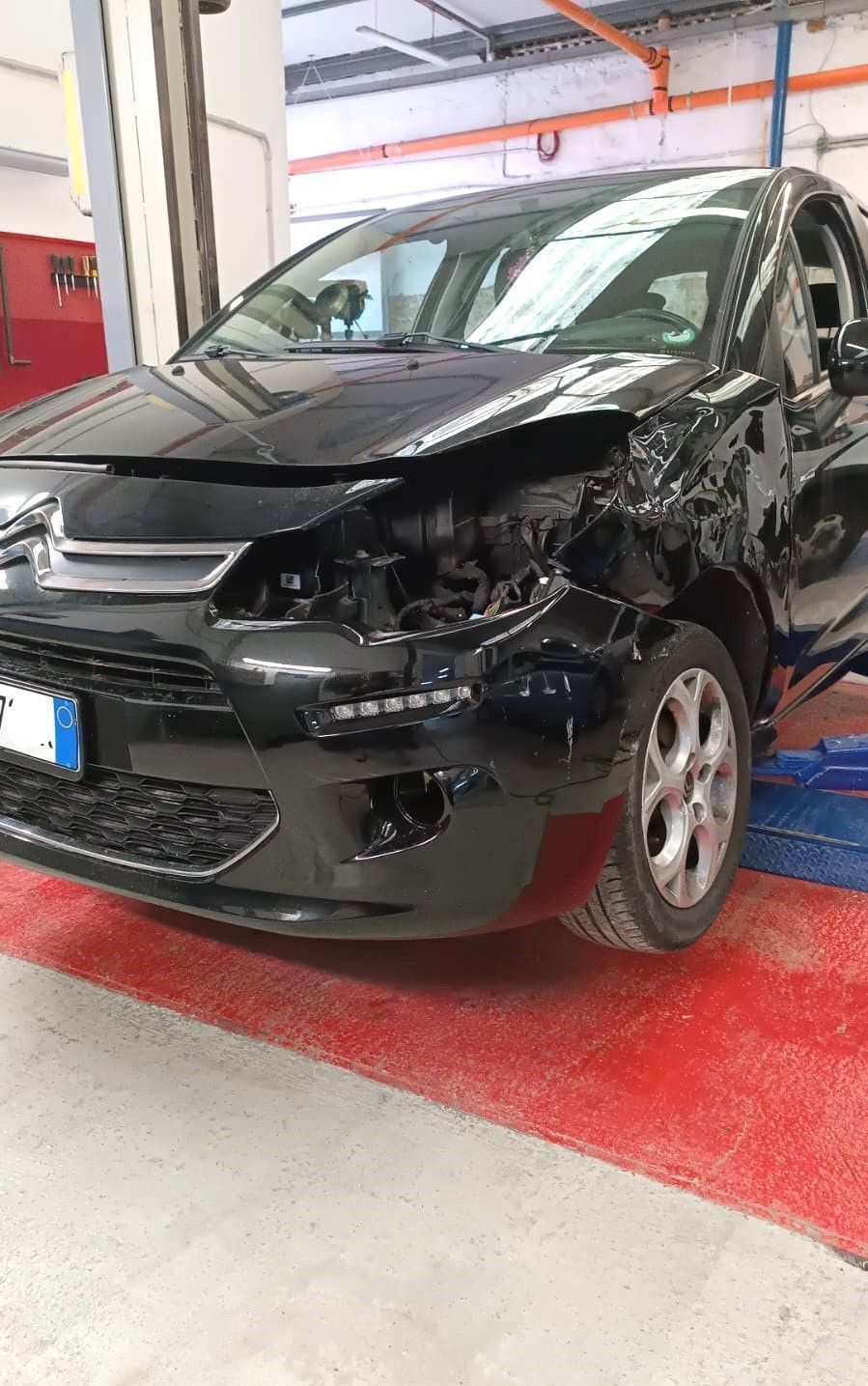 Auto nera con gravi danni alla parte anteriore, parcheggiata in un garage o in un'officina.
