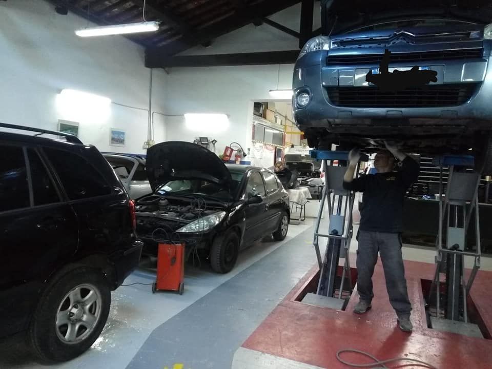 Officina meccanica con auto sui ponti sollevatori e un meccanico al lavoro sotto un veicolo blu.