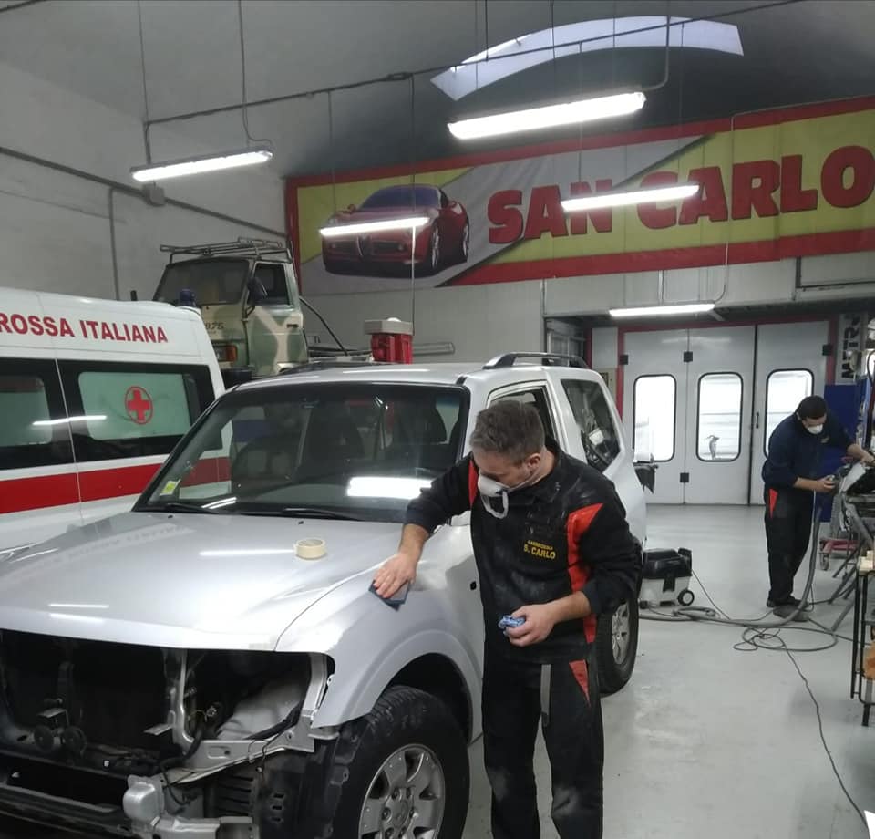 Un meccanico lavora su un SUV bianco in un'officina di carrozzeria con l'insegna rossa