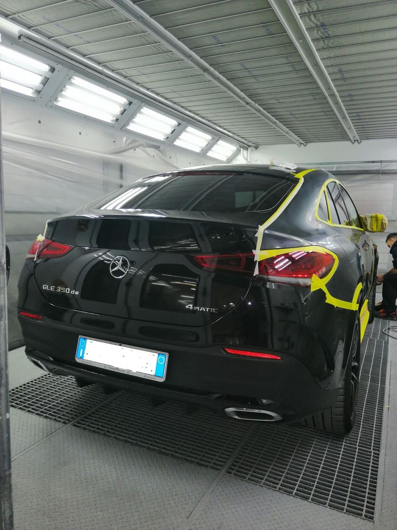 SUV nero in officina, con nastro giallo a segnalare i danni sul retro e sul lato.