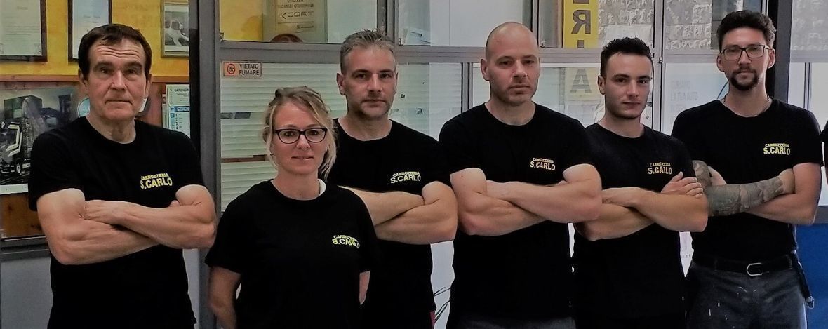 Cinque persone con indosso magliette nere, in piedi con le braccia incrociate, in una palestra o in uno studio.