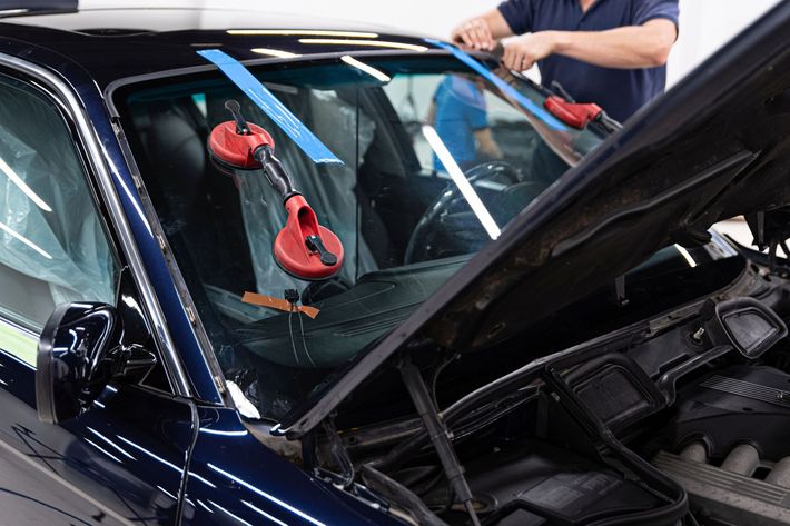 Riparazione del parabrezza di un'auto blu con strumenti a ventosa, con il cofano aperto.