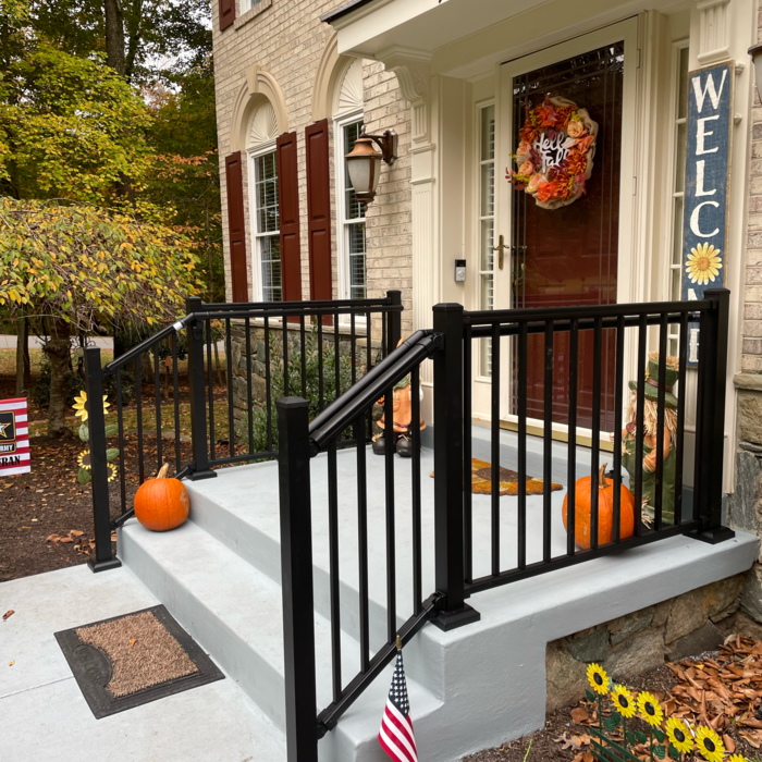 Black railing frames a front porch with pumpkins and a welcome wreath.