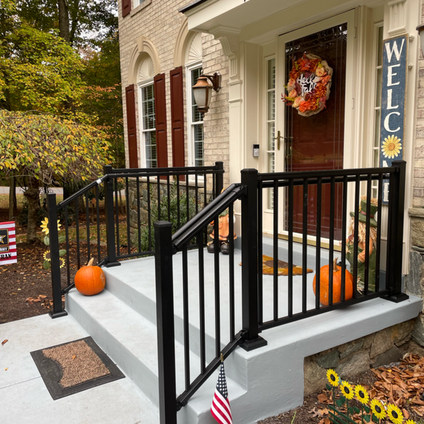 Black railing frames a front porch with pumpkins and a welcome wreath.