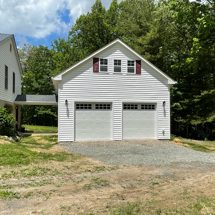 White two-car garage with two doors, two windows, and red shutters, connected to a house via a covered walkway.
