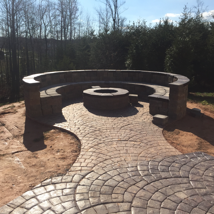 Circular stone fire pit with surrounding bench on a patterned patio.