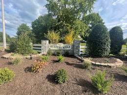 Sign for Hunters Mill, with stone pillars, surrounded by landscaping and fence.