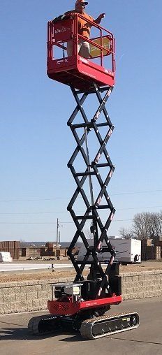 Red scissor lift extended outdoors on a construction site under a clear sky