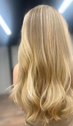 Blonde wavy hair seen from behind, lit by bright overhead lights.