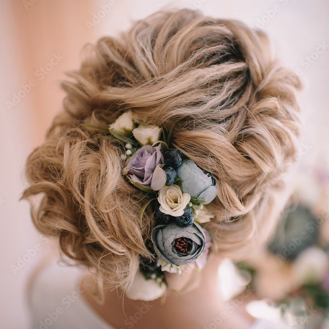 Blonde updo with pastel floral hair accessories against a soft pink background