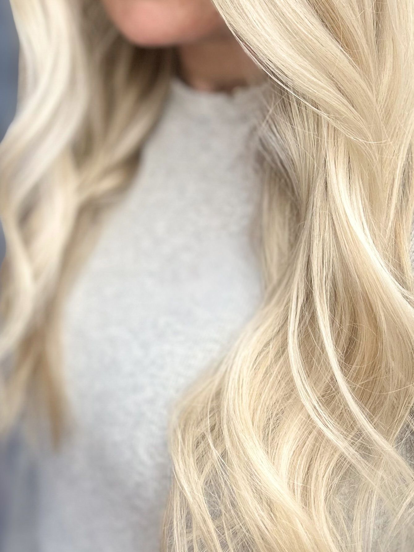 Close-up of wavy platinum blonde hair over a light gray sweater