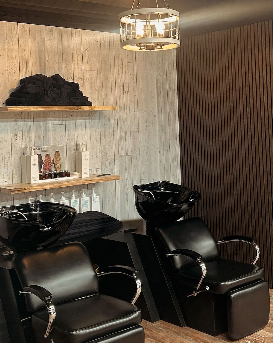 Modern salon with two black shampoo chairs, wood wall, shelves, and a hanging light