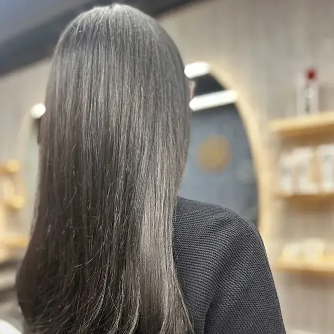 Person with long straight dark hair seen from behind in an indoor salon setting.