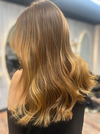 Back view of long, wavy light brown hair with blonde highlights in a salon setting