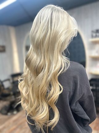 Long wavy blonde hair with subtle highlights, shown from the back in a salon setting