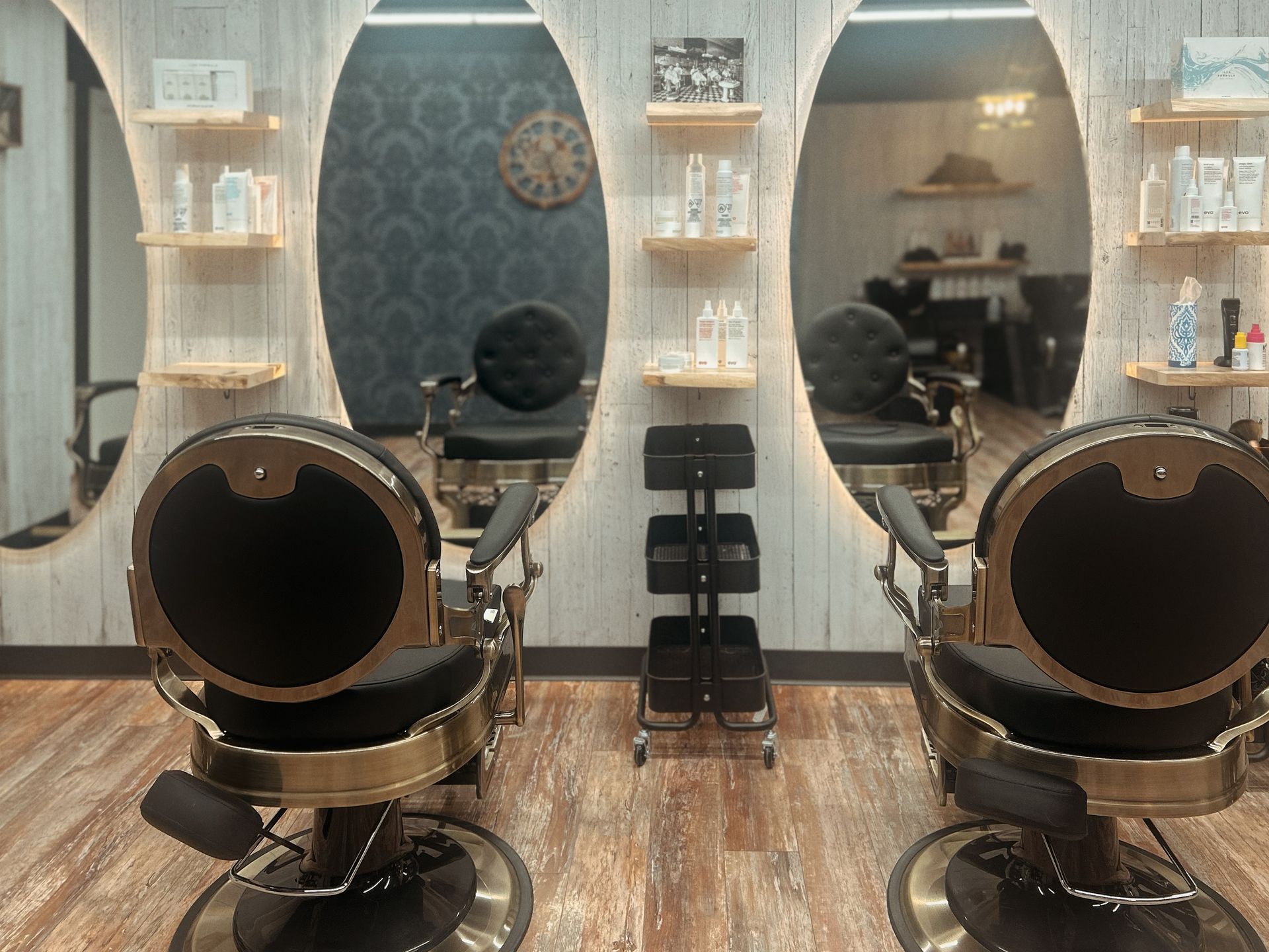 Modern salon with two black styling chairs, mirrors, shelves, and wood flooring