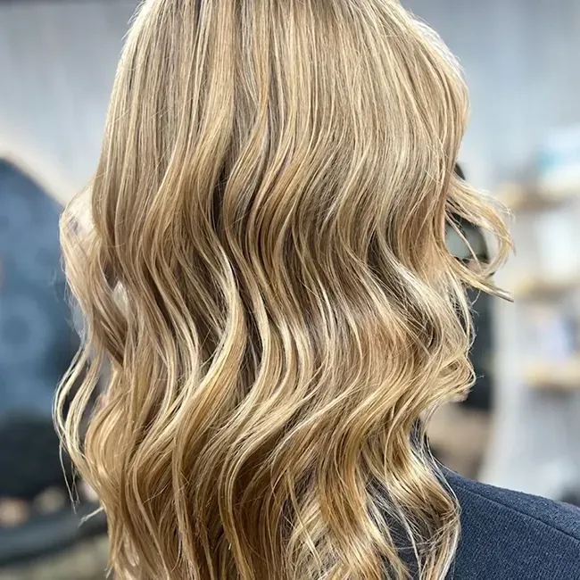 Close-up of wavy blonde hair from the back against a blurred indoor background