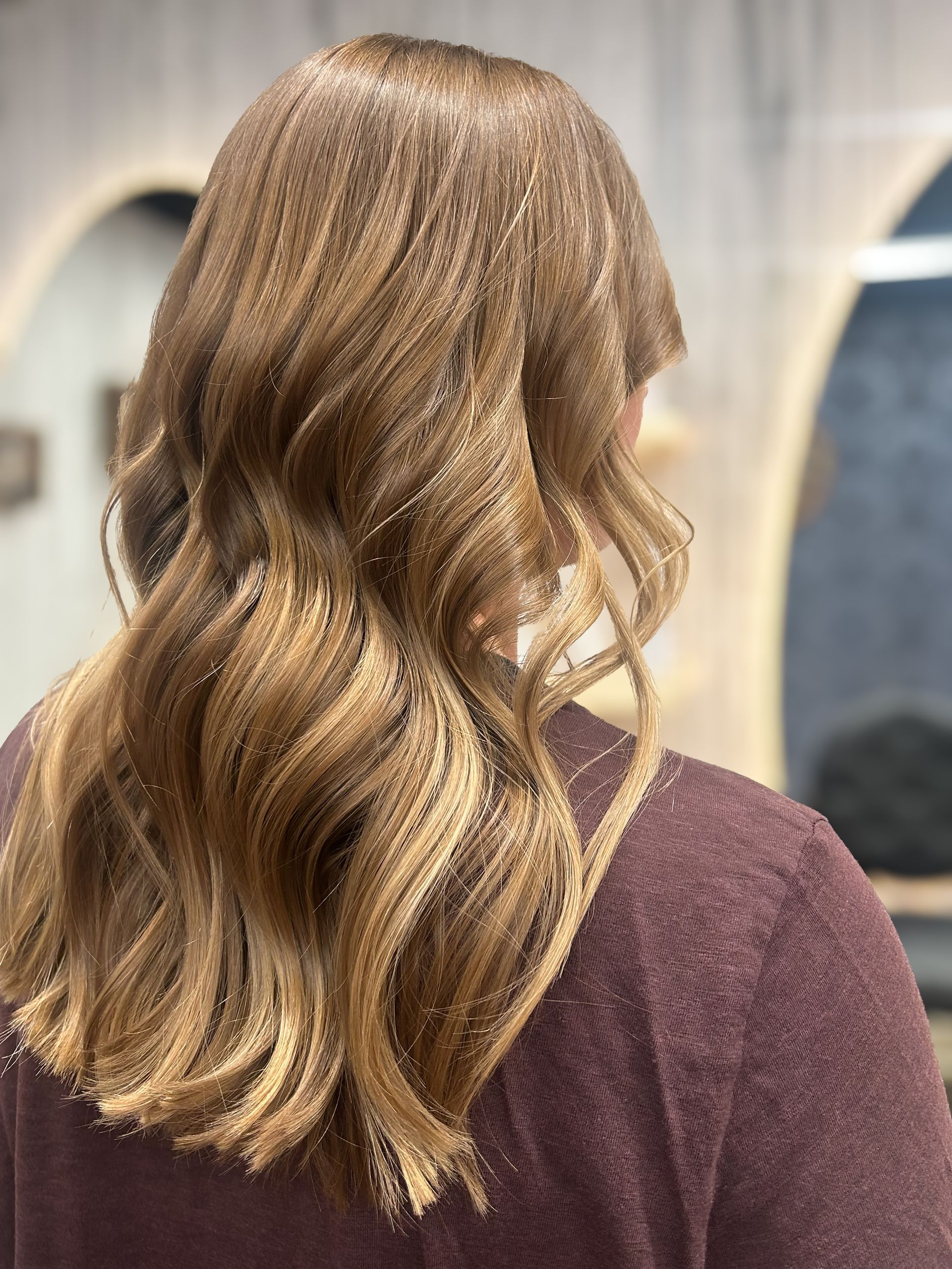 Back view of a person with wavy blonde hair wearing a purple sweater indoors