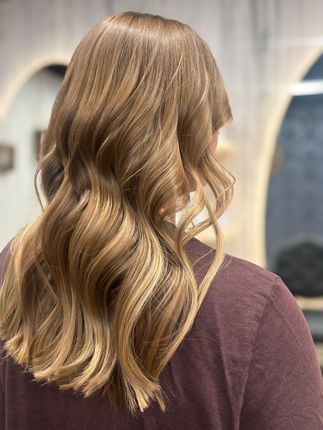 Wavy blonde hair falling over a maroon top, viewed from behind in a softly lit indoor setting