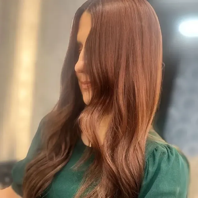 Woman with long auburn hair in a green top, softly lit indoors, looking downward.