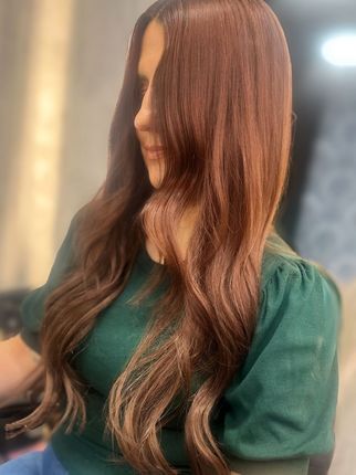 Woman with long wavy auburn hair in a green top, standing indoors in soft light.