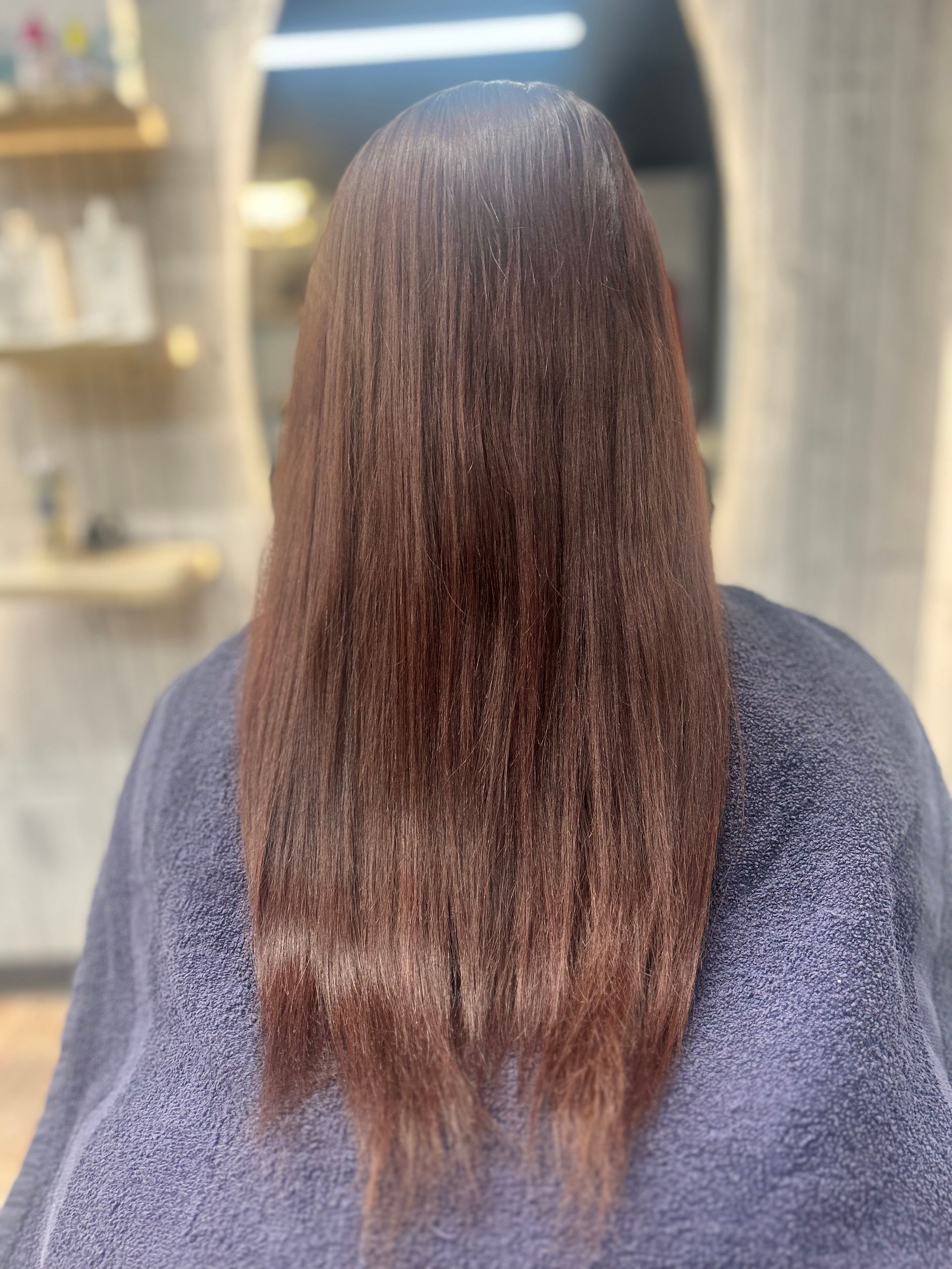 Back view of long, straight brown hair with slightly frayed ends in a salon setting