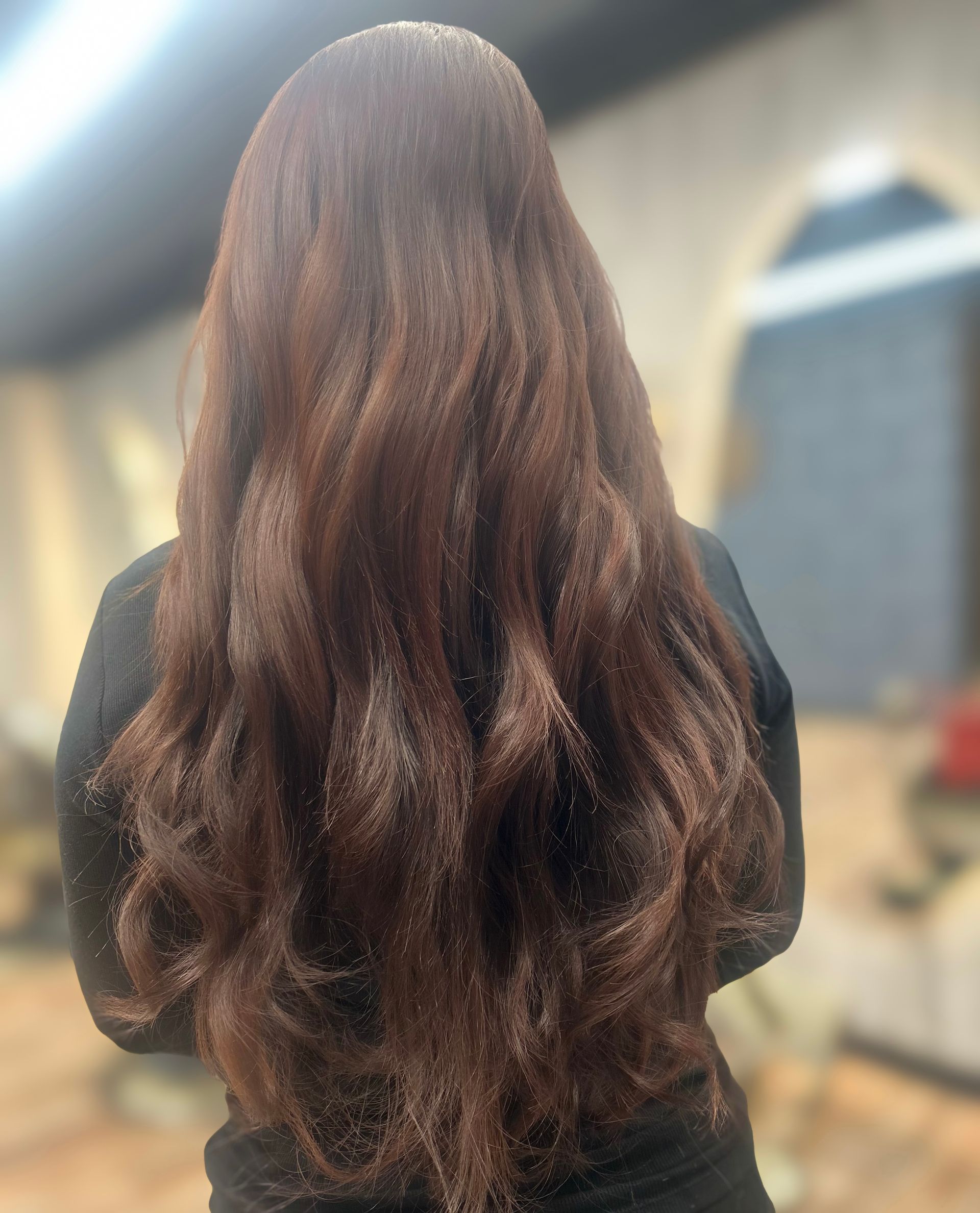 Long wavy brown hair seen from behind in a softly lit indoor setting