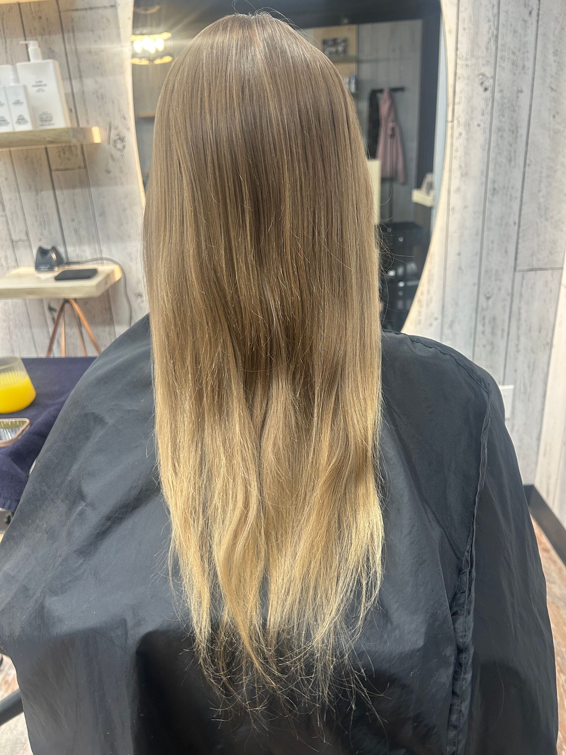 Long straight brown hair with blonde ends draped over a black salon cape in a hair salon.
