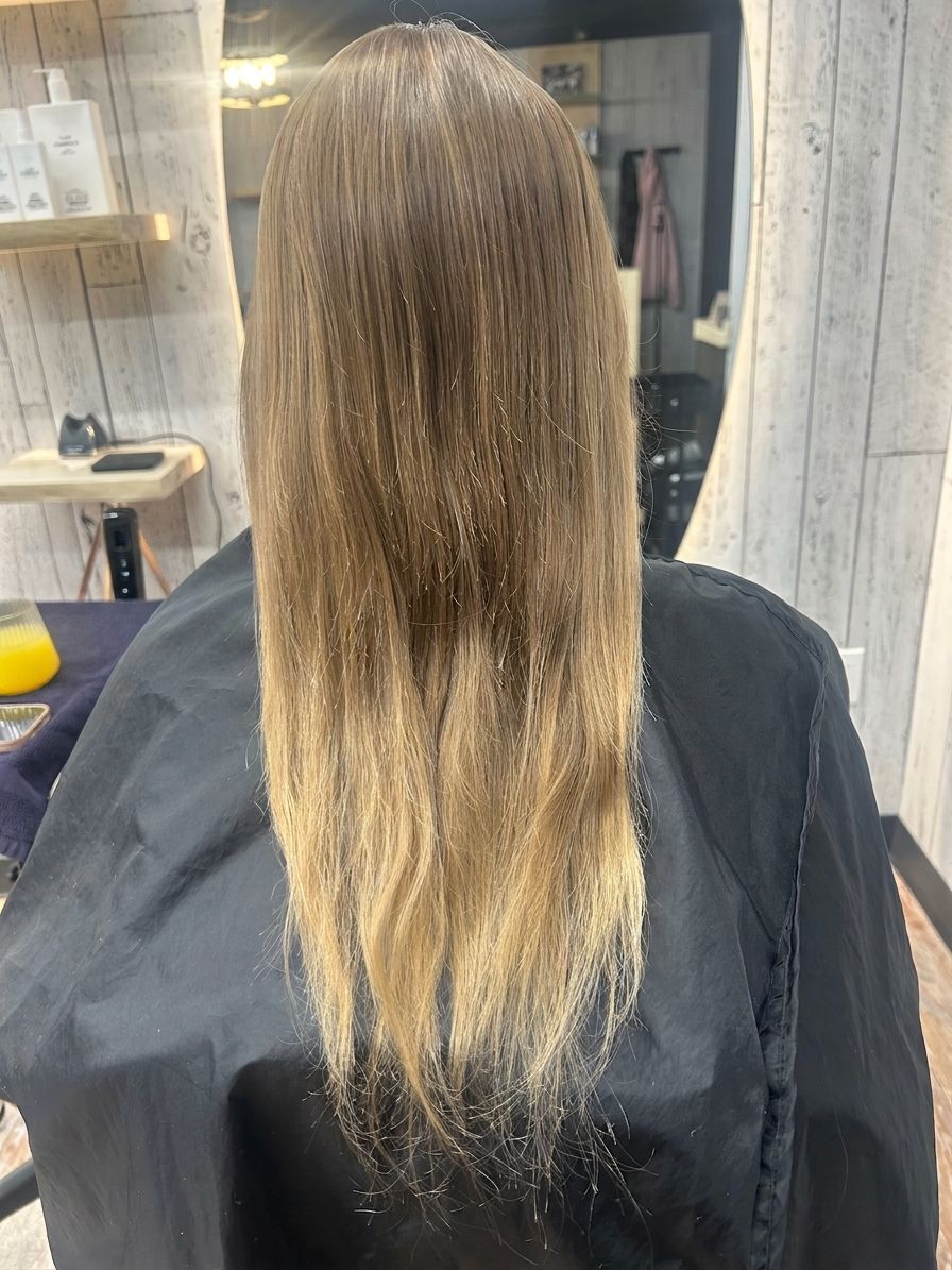 Back view of long straight brown hair fading to blonde at the ends in a salon chair