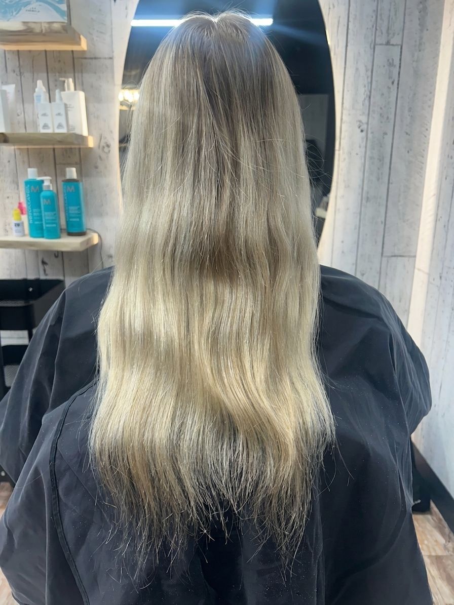 Long blonde hair with dark roots and lighter ends, viewed from behind in a salon chair.