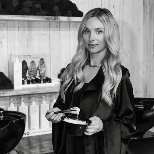 Woman holding a product in a salon, standing beside shelves of hair care items.