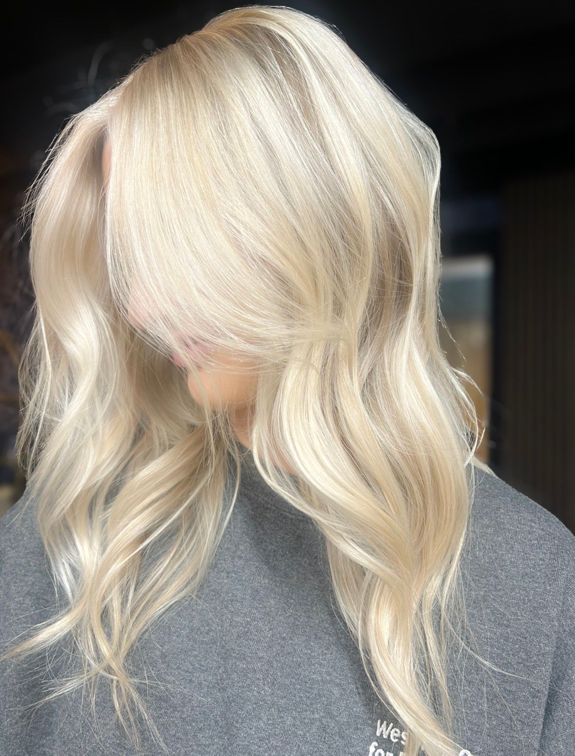 Blonde wavy hair styled in loose layers over a gray top against a dark background