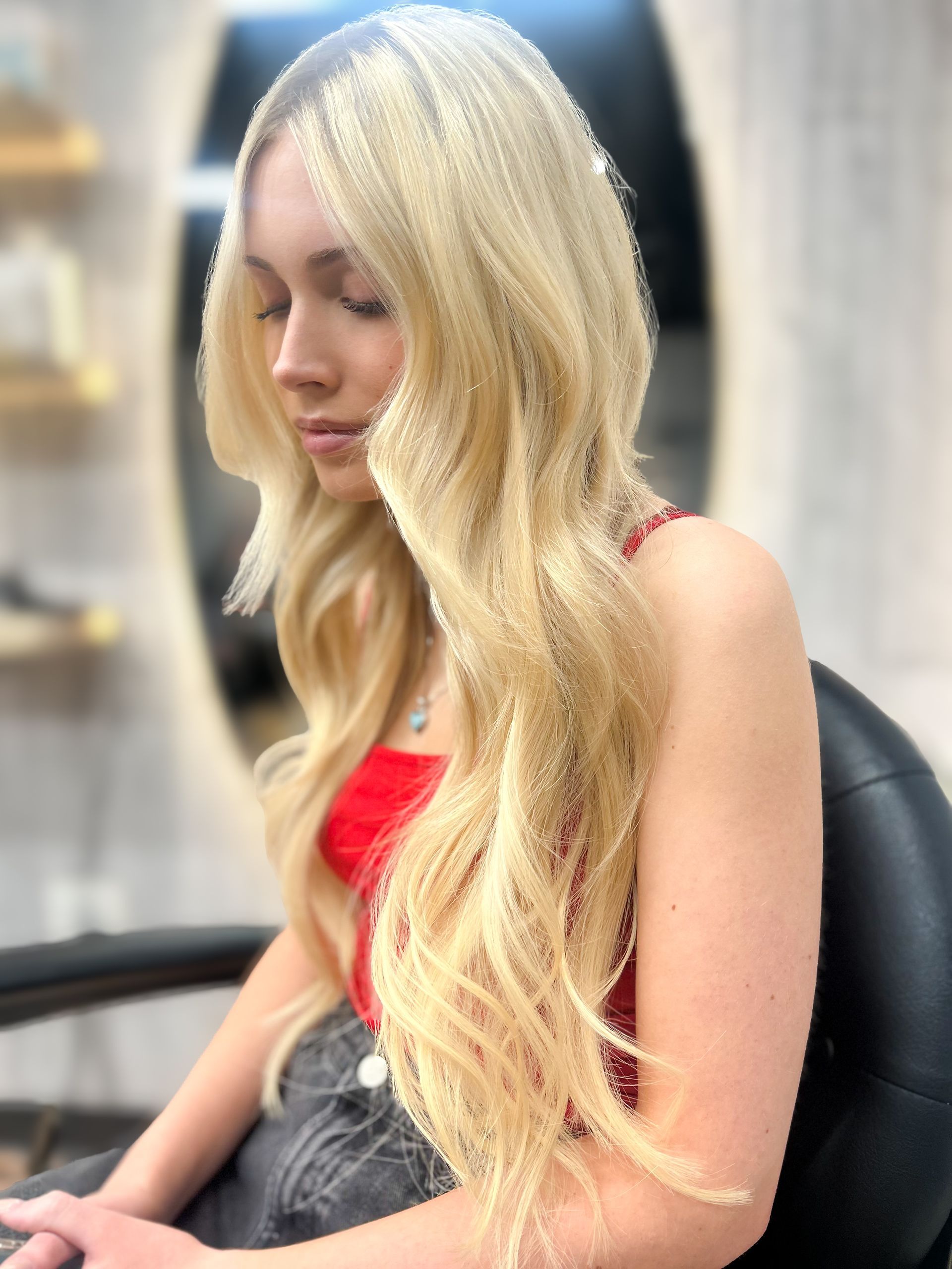 Blonde woman in a red top sitting in profile, looking down indoors.